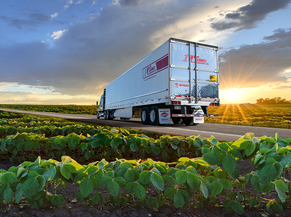 McConnell Transport truck driving on road with farm fields of produce on either side