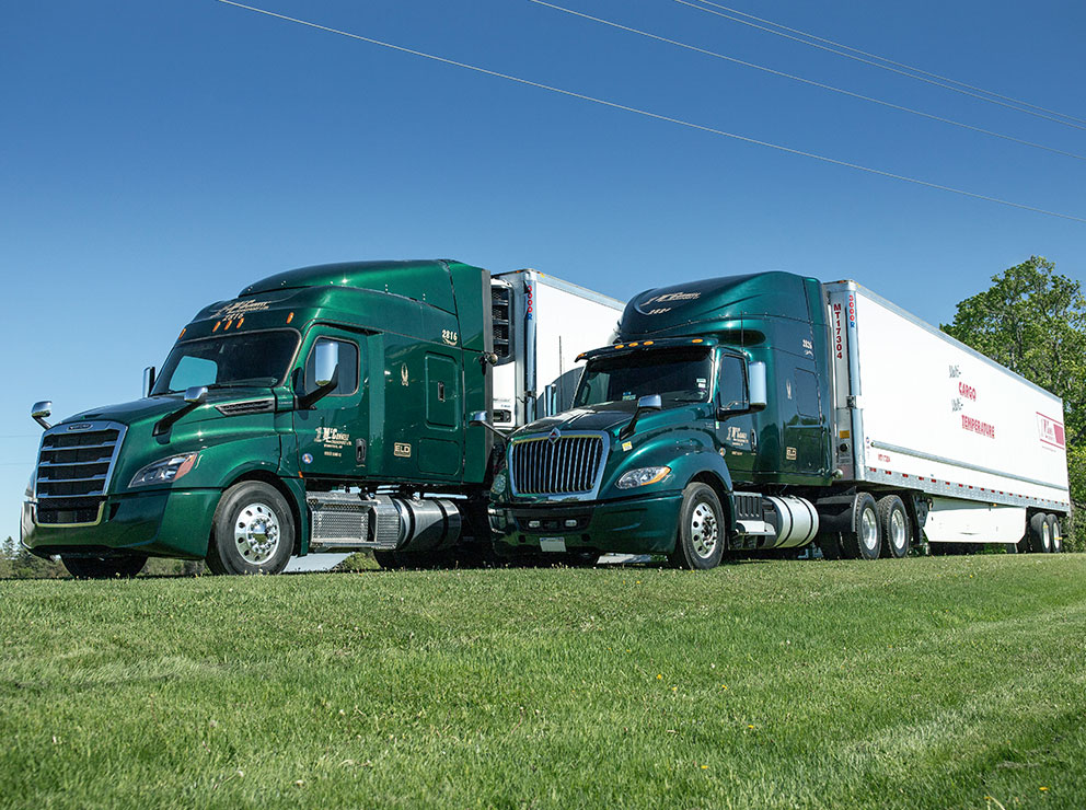 Two McConnell Transport trucks parked side by side on grass, with trees in the background